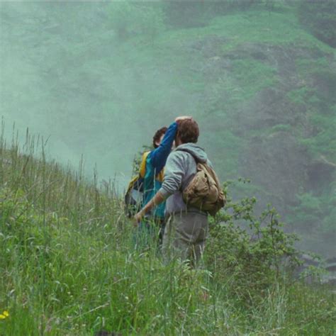 Two People Walking Up A Hill With Backpacks On Their Back In The Fog