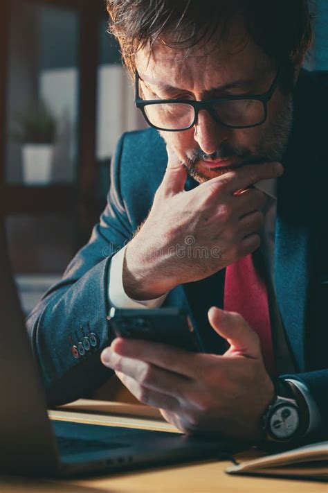 Businessman Using Mobile Phone At Work Desk In Office Checking