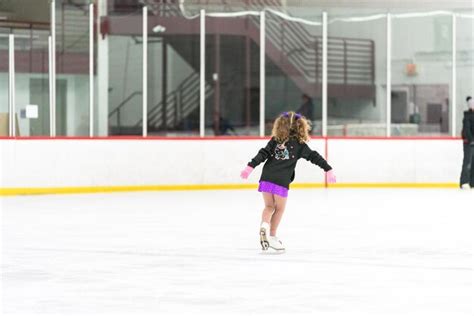 Menina praticando patinação artística em uma pista de patinação no gelo