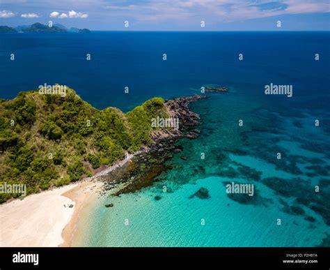 Aerial drone view of an empty, beautiful tropical beach surrounded by coral reef and greenery ...