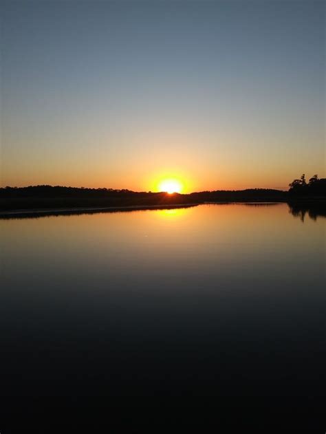 The Sun Is Setting Over Water With Trees In The Background