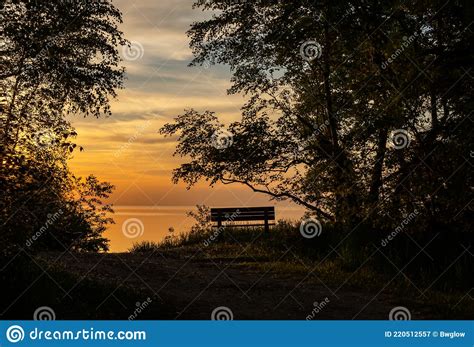 Lonely Park Bench Overlooking Setting Sun And Calm Lake Stock Image