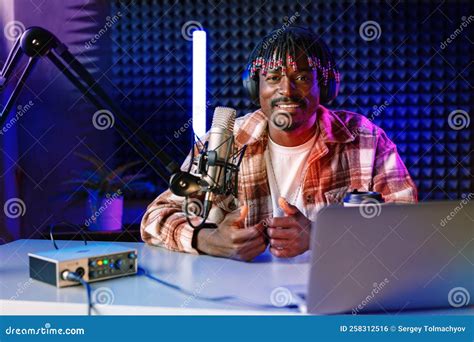 African Radio Host Sitting At Desk Recording In Studio With Microphone