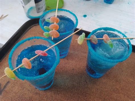 Three Glasses Filled With Blue Liquid And Gummy Bears On Top Of A