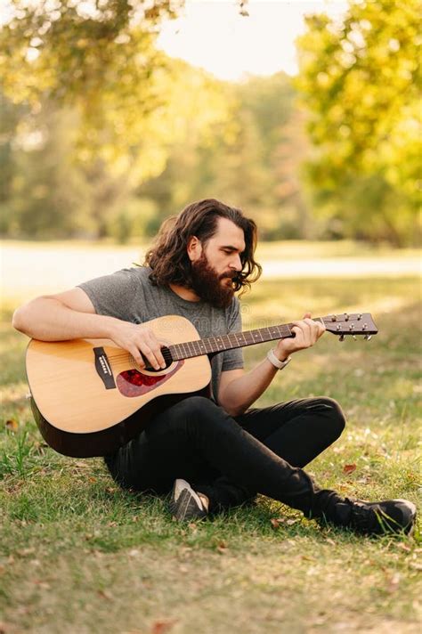 Vertical Shot Of A Handsome Bearded Man Playing Guitar While Sitting In