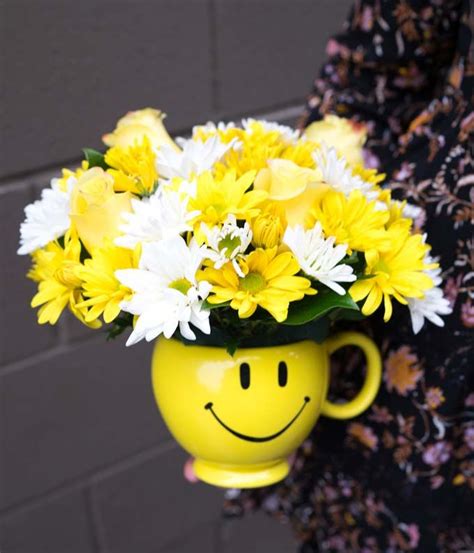 A Yellow Smiley Face Vase With White And Yellow Flowers In It Is Held