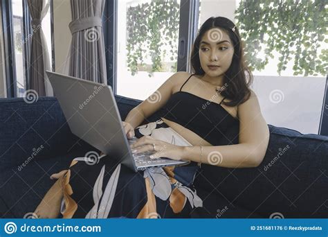 A Young Asian Woman Who Spend Her Time At Home Sitting On A Cozy Sofa