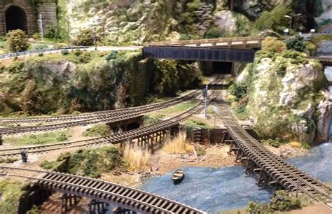 A Model Train Set Is Shown On The Tracks Next To A River And Bridge With Boats