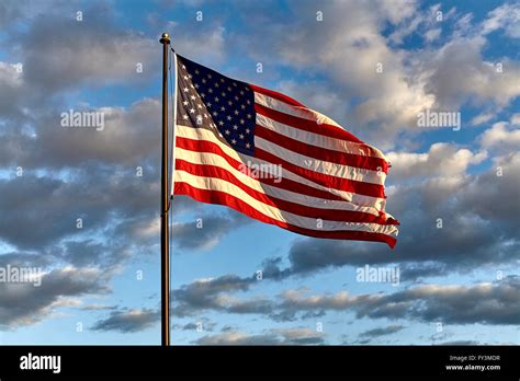 American Flag On Flagpole Waving In The Wind Against Clouds Blue Sky