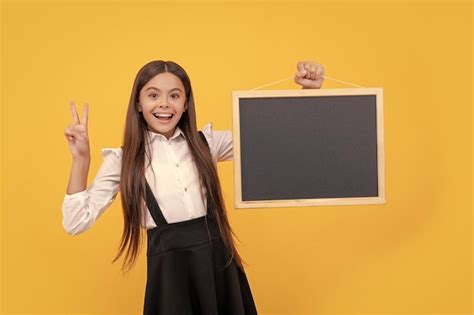 Niña adolescente sonriente en uniforme sostiene la pizarra de la