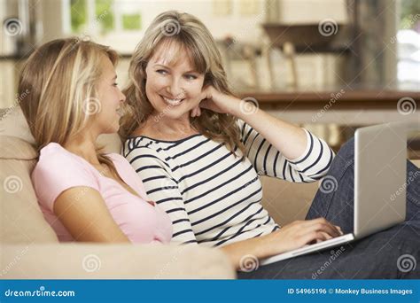 Mother With Teenage Daughter Sitting On Sofa At Home Using Laptop Stock