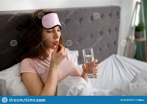 Sleepy Young Woman With Glass Of Water Taking Pill In Bed At Home Copy