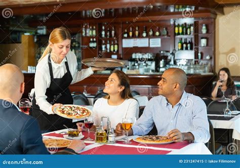 Young Waitress Serving Ordered Pizza To Guests In Restaurant Stock