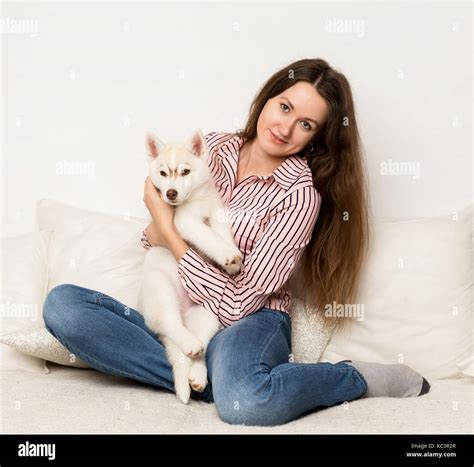 Happy Beautiful Woman Hugging Puppy Husky Girl Sitting On A Sofa With