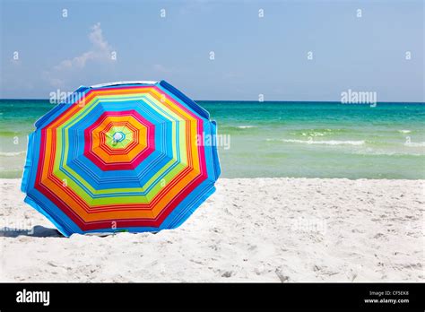 Colorful Umbrella Sitting On A Sandy Beach With The Ocean And Blue Sky In The Background Stock