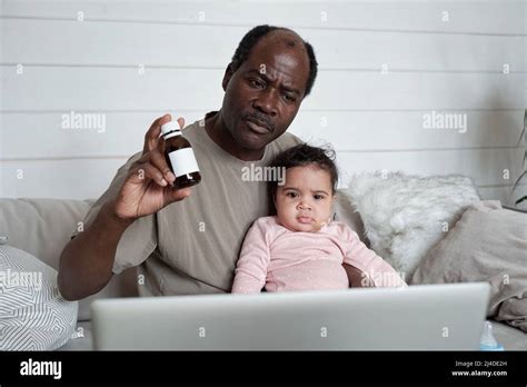 Modern Mature Black Man Sitting On Sofa In Front Of Laptop With Baby Daughter On His Lap Having