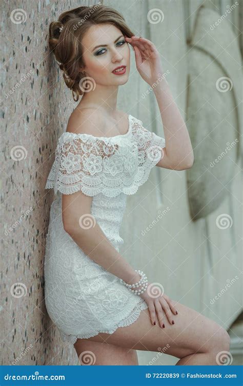 Beautiful Stylish Girl Posing In Short White Dress Against Stone Wall