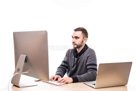 Businessman Sitting Behind Desk At Work Looking At Monitor And Laptop