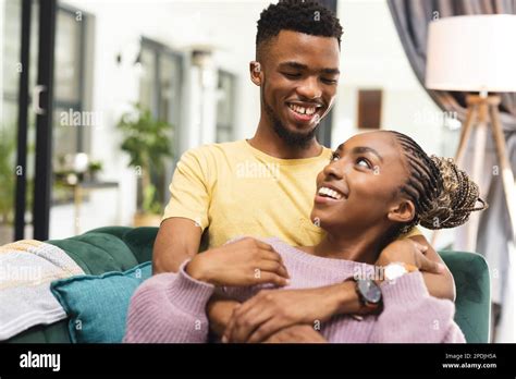 Happy African American Couple Sitting On Sofa And Embracing In Living