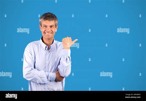 Mature Businessman Pointing Thumb Aside Showing Empty Space Blue