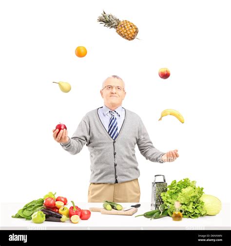 A Smiling Mature Man Juggling Fruits Behind A Table Full With