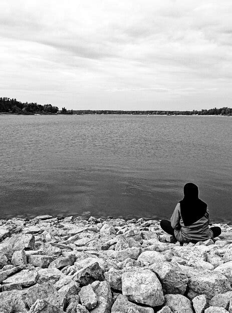 Premium Photo Rear View Of Woman Sitting On Rocks At Lake Shore