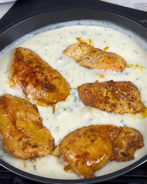 Some Chicken Is Being Cooked In A Skillet On The Stove With White Sauce