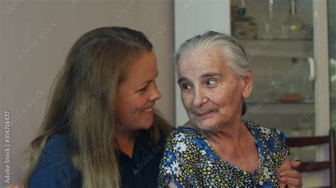 A Young Woman Hugs Her Ninety Year Old Grandmother At Home On The Couch