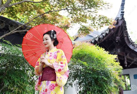 Traditional Asian Japanese Beautiful Woman Bride Wears Kimono With Red Umbrella In Front Of A