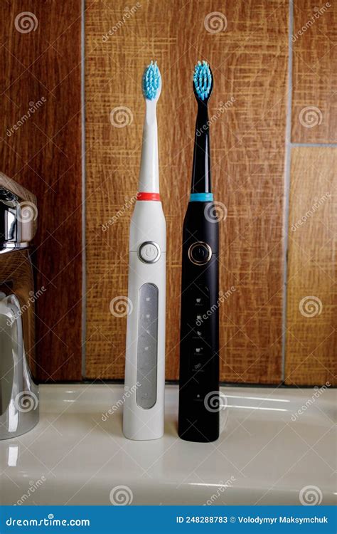 Two Electric Toothbrushes On The Sink In The Bathroom With A Gray Soap