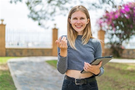 Junge blonde frau hält ein tablet im freien und lädt mit der hand zum kommen ein glücklich