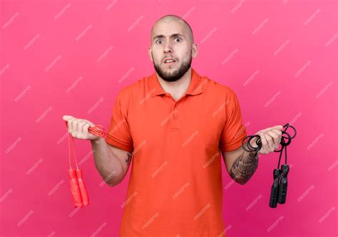 Free Photo Confused Young Sporty Man Holding Jump Ropes Isolated On Pink