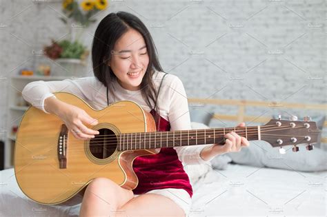 Cute And Happy Smiling Asian Girl Playing Acoustic Guitar In Bedroom