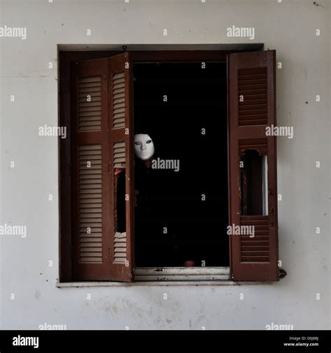 Man With White Mask By The Broken Window Shutter Of An Abandoned House