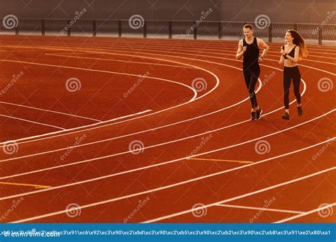 Young Man And Woman Running On Race Track In Modern Stadium Stock