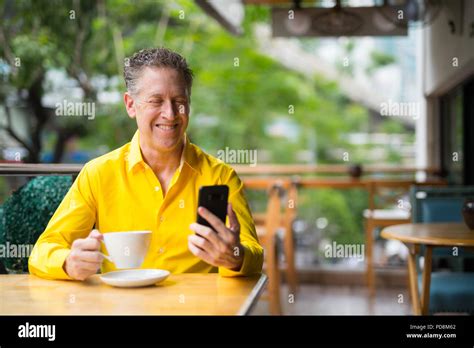 Mature Handsome Man Sitting In Coffee Shop While Using Mobile Phone