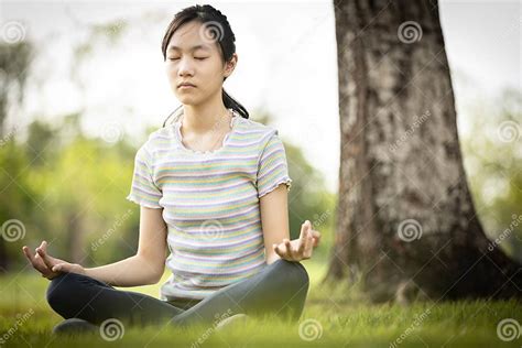 Happy Woman Meditating In Yoga Pose Or Lotus Position On The Green