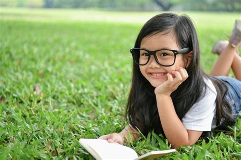 Premium Photo Portrait Of Smiling Girl Reading Book While Lying On Field