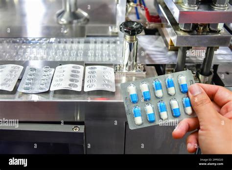 Hand Holding Blue Capsule Pack At Medicine Pill Production Line