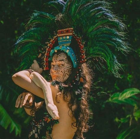 A Woman In An Elaborate Headdress With Feathers On Her Face And Hands