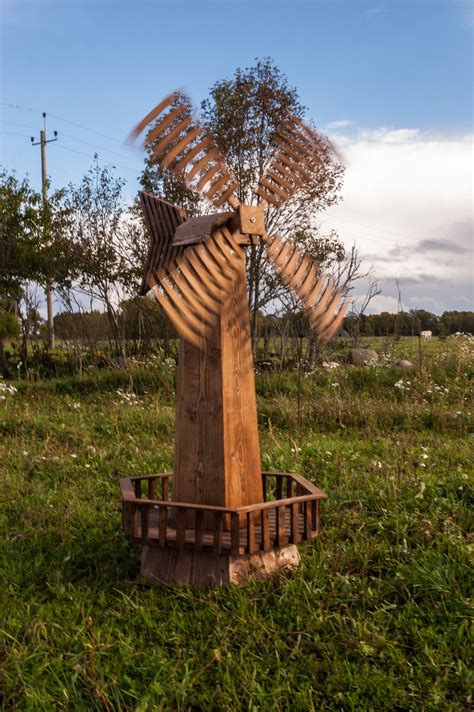 A Wooden Windmill Sculpture Sitting In The Middle Of A Field