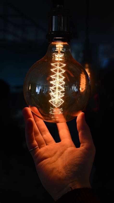 A Person Holding A Light Bulb In The Dark With Their Hand On Top Of It