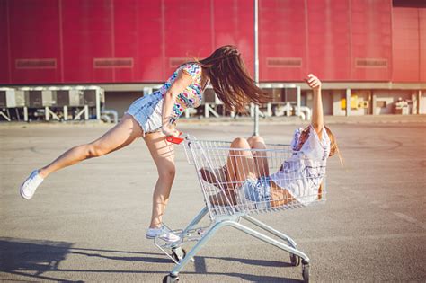 Two Girls Playing With Shopping Cart Two Young Women Spinning And