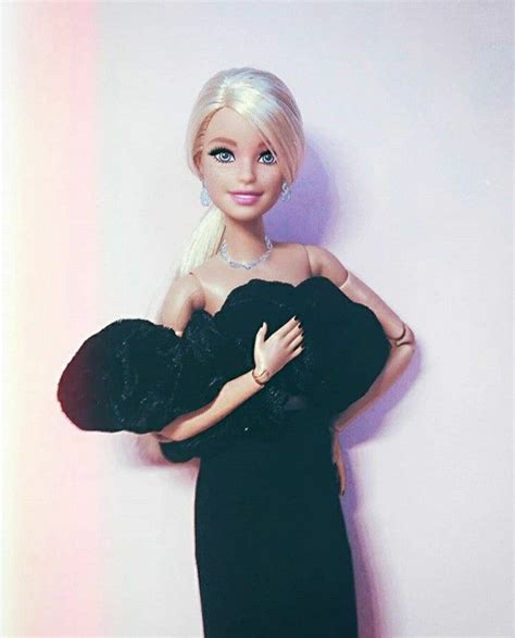 A Barbie Doll Wearing A Black Dress And Holding A Teddy Bear In Her