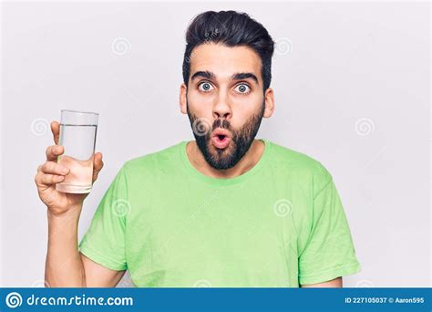 Young Handsome Man With Beard Drinking Glass Of Water Scared And Amazed