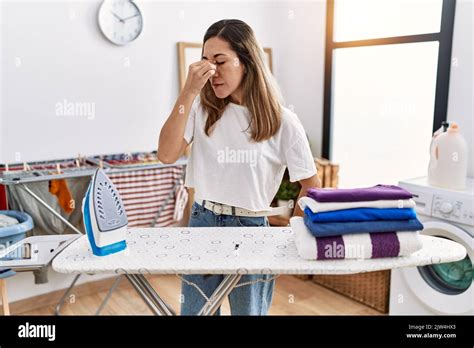 Mujer joven hispana planchando ropa en la lavandería cansada frotándose