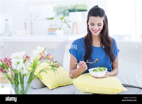 Smiling Beautiful Brunette Sitting On The Couch And Eating Salad Stock