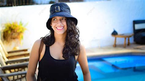 Smiling Latin Girl With Hat By Pool On Muskoka Chairs Photo Background