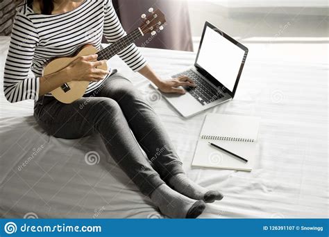 Happy Young Asian Woman Playing Ukulele Sitting On Bed In Bedroom