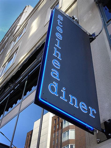 A Blue Neon Sign Hanging From The Side Of A Building Next To A Tall